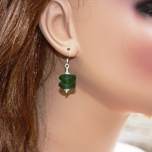 May include: A pair of dangle earrings with a dark green glass bead. The bead is faceted and has a geometric shape.