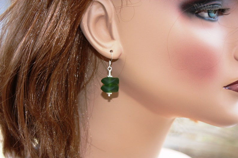 May include: A pair of dangle earrings with a dark green glass bead. The bead is faceted and has a geometric shape.