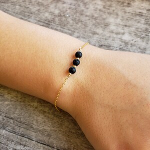 May include: A gold chain bracelet with three black lava rock beads.