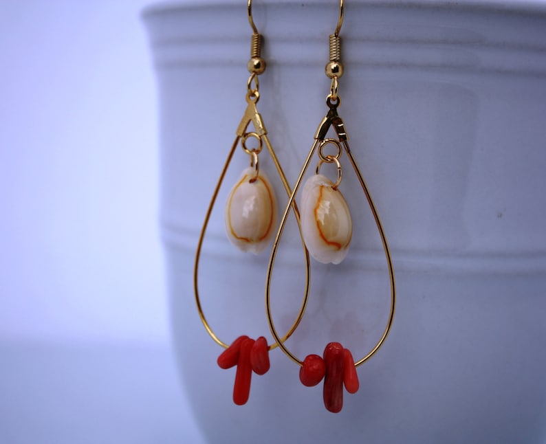 May include: Gold teardrop earrings with a white seashell charm and red coral accents.