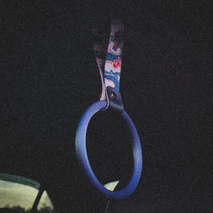 Op de afbeelding: Een blauwe auto-interieurhandgreep met een patroonband. De handgreep heeft een cirkelvorm en de band heeft een ontwerp met rode, witte en blauwe elementen. De achtergrond is donker, wat een contrast creëert.