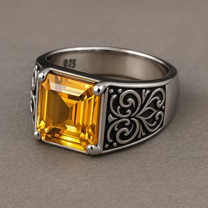 Peut inclure: Bague en argent avec une grande pierre jaune rectangulaire. La bague présente un motif de filigrane noir orné sur les côtés et le chiffre "075" est visible sur le bandeau. La pierre est d'un jaune doré vif.