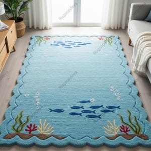Puede incluir: Una alfombra rectangular azul claro con borde festoneado. La alfombra presenta una escena submarina con bancos de peces azules, algas y coral. La alfombra está hecha de un material suave y texturizado y está diseñada para una sala de estar o dormitorio.