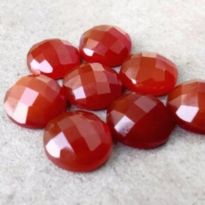 May include: A cluster of faceted, round, red gemstones. The gemstones have a polished, reflective surface and are arranged in a loose cluster. The colour is a deep, rich red, with variations in tone due to the facets.