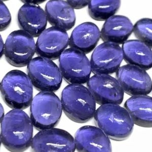 Peut inclure: Gros plan sur de nombreuses pierres précieuses ovales indigo foncé. Les pierres polies ont une surface lisse et réfléchissante, avec de légères variations de couleur. Les pierres sont disposées de près, remplissant le cadre.