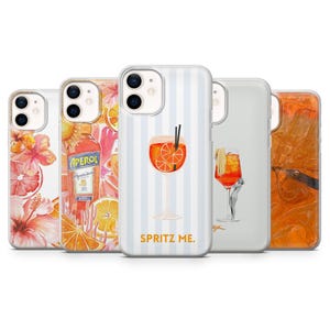 May include: A collection of phone cases with various designs. One case features a cocktail illustration with the text "SPRITZ ME." Other cases display floral, fruit, and Aperol bottle designs. The cases are made of a clear material.