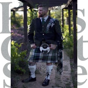 Puede incluir: Un hombre con un atuendo tradicional escocés de kilt. El atuendo incluye una chaqueta negra, corbata verde y kilt a cuadros verdes y blancos. Un sporran blanco cuelga de la cintura. Calcetines blancos y zapatos negros completan el look.
