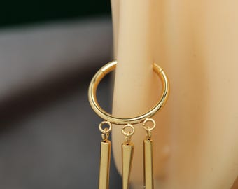 May include: A gold-coloured hoop earring with three dangling charms. Two charms are rectangular, and one is a pointed cone shape. The earring is attached to a light-coloured surface.