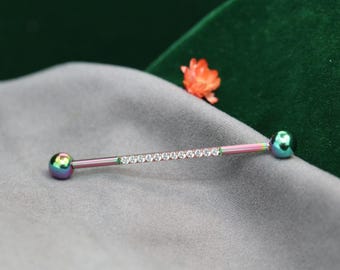May include: A body piercing barbell with a rainbow iridescent finish. The barbell features a row of small, clear rhinestones down the center and rounded ends. The ends have a matching iridescent finish.