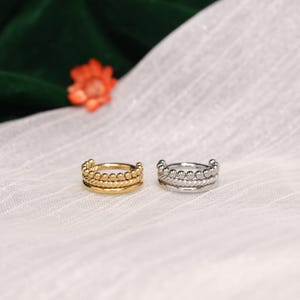 May include: Two circular ear cuffs, one in a gold tone and one in a silver tone. Each cuff features a triple-band design consisting of a beaded outer edge, a twisted middle rope texture, and a smooth inner band, creating a layered appearance.