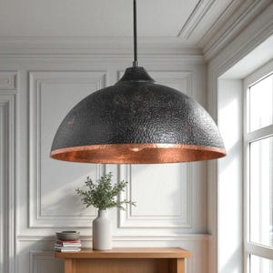 May include: A large dome-shaped pendant light fixture featuring a textured black exterior finish and a contrasting polished copper interior lining. The lamp hangs from a single black cord and provides a wide downward light projection.