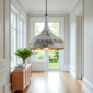 Könnte beinhalten: Eine weiße und goldfarbene Pendelleuchte hängt in einem Flur. Die Leuchte hat eine Used-Optik mit kupferfarbenem Innenraum. Der Flur hat Parkettböden, weiße Wände und einen Holzschrank mit einer Vase mit Grünzeug.