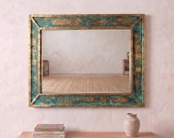 May include: A rectangular wall mirror featuring a wide, textured frame with a weathered patina finish in shades of teal, green, and metallic gold. The frame has a distinct border with visible rivet-like details at the corners and along the edges.