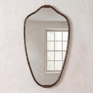 May include: A wall mirror with an irregular, teardrop-shaped frame in a dark bronze finish. The reflective glass surface shows a clear view of a window with white glazing bars. The frame features a smooth, continuous metal border with a small horizontal connector at the top and bottom centre points.