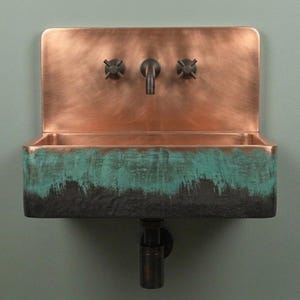 Peut inclure: Un évier mural doté d'un dosseret et d'une vasque en cuivre poli. L'extérieur avant présente une finition texturée avec un dégradé passant du gris anthracite foncé à une patine turquoise vive. Il comprend un robinet central et deux boutons.
