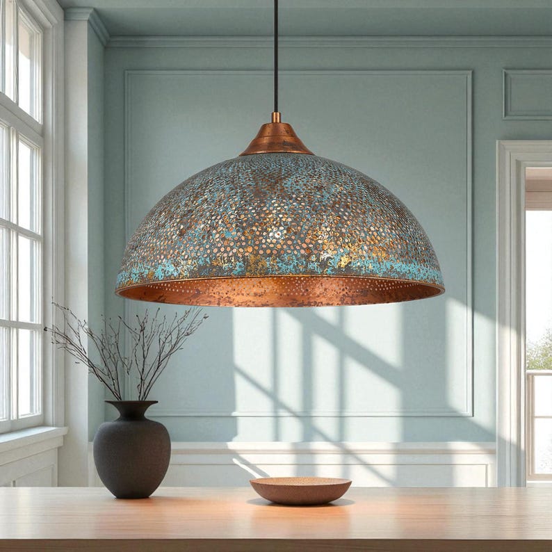 May include: A dome-shaped pendant light with a copper finish and a distressed blue-green patina. The light fixture hangs from a black cord and is suspended above a wooden table. The light has a perforated design and is a decorative element.