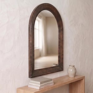 May include: An arched wall mirror featuring a dark, textured copper-toned metal frame. The mirror has a smooth, reflective glass surface with a rounded top edge and straight sides, mounted vertically to display a clear, undistorted reflection.