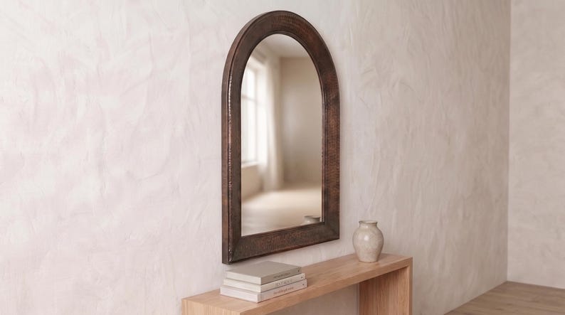 May include: An arched wall mirror featuring a dark, textured copper-toned metal frame. The mirror has a smooth, reflective glass surface with a rounded top edge and straight sides, mounted vertically to display a clear, undistorted reflection.