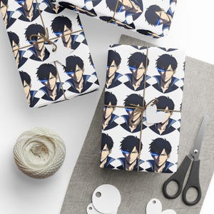 May include: Gift wrapping paper featuring a repeating pattern of a character with black hair and blue glowing eyes. The wrapped gifts are tied with twine and a small heart-shaped tag. A ball of twine, scissors, and blank tags are also visible.