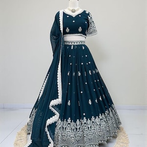 May include: A teal-colored, embroidered formal dress with a matching shawl. The dress features intricate silver embroidery on the bodice, waist, and skirt. The shawl has a white lace trim. The dress is displayed on a mannequin.