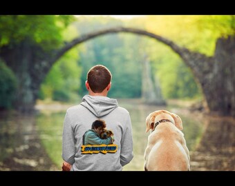 May include: A light grey hoodie featuring a graphic of a person embracing a dog, with the text "MY BESTEST FRIEND". A yellow Labrador Retriever sits nearby. The background shows a stone bridge and a lake.