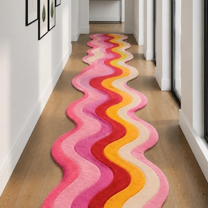 Könnte beinhalten: Ein farbenfroher, wellenförmiger Teppich in einem Flur. Der Teppich hat ein lebendiges Design mit Streifen in Pink, Rot, Gelb und Beige. Die einzigartige Form und Farbpalette des Teppichs verleihen dem Raum eine moderne Note.