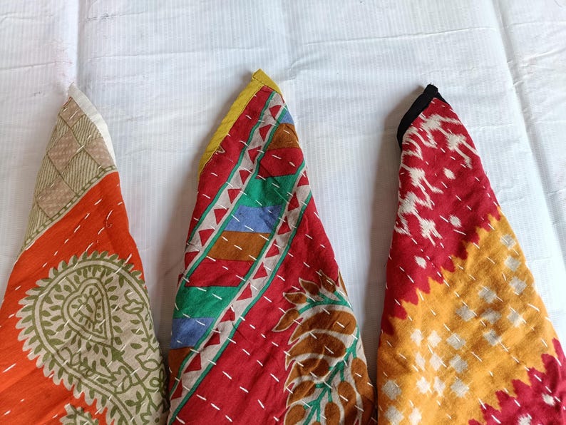 Puede incluir: Tres piezas de tela plegadas con patrones y costuras coloridas. Las telas presentan tonos de naranja, rojo, amarillo, verde y marr&oacute;n. Las costuras blancas crean un efecto de contraste. Los art&iacute;culos est&aacute;n dispuestos sobre una superficie blanca.