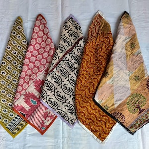 Könnte beinhalten: Fünf bunte Stoffservietten mit Mustern, in einer Reihe angeordnet. Die Servietten weisen verschiedene Designs auf, darunter Blumen- und geometrische Muster, in Grün-, Rot-, Schwarz- und Orangetönen. Jede Serviette ist zu einem Dreieck gefaltet.