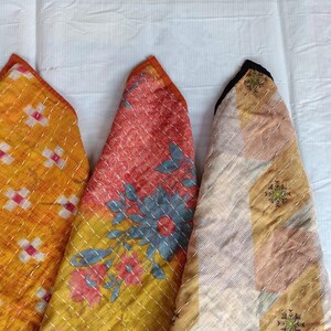Pode incluir: Close-up de tr&ecirc;s pe&ccedil;as de tecido acolchoado colorido. As pe&ccedil;as s&atilde;o triangulares com estampas florais laranja, vermelha e amarela. As bordas s&atilde;o aparadas com tecido laranja e costuradas com linha branca. Os tecidos est&atilde;o em um fundo branco.