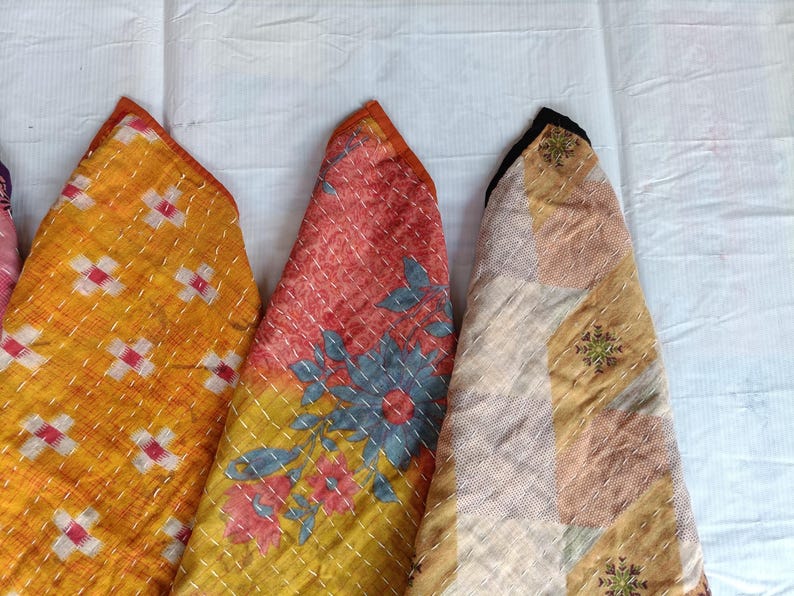 Pode incluir: Close-up de tr&ecirc;s pe&ccedil;as de tecido acolchoado colorido. As pe&ccedil;as s&atilde;o triangulares com estampas florais laranja, vermelha e amarela. As bordas s&atilde;o aparadas com tecido laranja e costuradas com linha branca. Os tecidos est&atilde;o em um fundo branco.