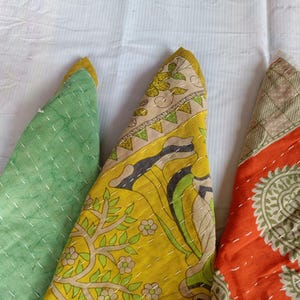 Puede incluir: Primer plano de tres piezas de tela triangulares de colores. Una es verde, otra amarilla con un dise&ntilde;o floral y la tercera naranja con un estampado de cachemira. Todas las piezas tienen costuras blancas y ribete amarillo.