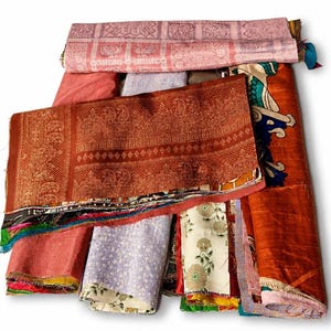 May include: A collection of folded fabric scraps featuring various patterns and colors, including a top layer with a pink elephant motif, a central rust-colored piece with intricate paisley designs, and other segments with floral and geometric prints.