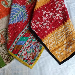 Puede incluir: Primer plano de piezas de tela coloridas y estampadas. Los textiles presentan tonos rojos, naranjas y amarillos con dise&ntilde;os intrincados, incluyendo patrones florales y geom&eacute;tricos. Los bordes est&aacute;n acabados con bordes contrastantes y costuras visibles.