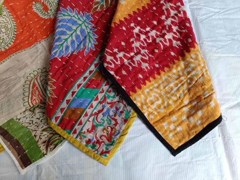 Puede incluir: Primer plano de piezas de tela coloridas y estampadas. Los textiles presentan tonos rojos, naranjas y amarillos con dise&ntilde;os intrincados, incluyendo patrones florales y geom&eacute;tricos. Los bordes est&aacute;n acabados con bordes contrastantes y costuras visibles.