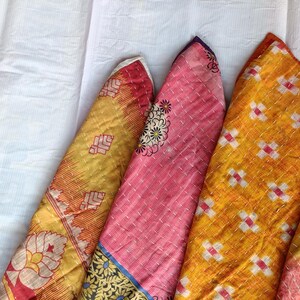 Pode incluir: Uma cole&ccedil;&atilde;o de pe&ccedil;as de tecido coloridas e dobradas. Os tecidos apresentam v&aacute;rios padr&otilde;es, incluindo desenhos florais e geom&eacute;tricos, em tons de amarelo, laranja e rosa. As pe&ccedil;as est&atilde;o dispostas sobre uma superf&iacute;cie branca, mostrando as texturas e cores.