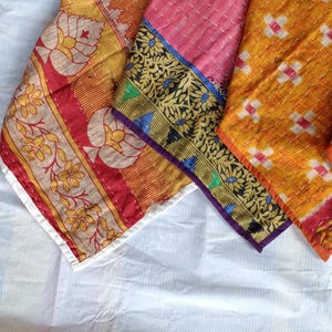 Pode incluir: Close-up de v&aacute;rios peda&ccedil;os de tecido coloridos e estampados. Os tecidos apresentam desenhos florais e geom&eacute;tricos em tons de amarelo, vermelho, rosa e laranja, com bordas decorativas. As pe&ccedil;as s&atilde;o costuradas, sugerindo um edredom ou arte t&ecirc;xtil.