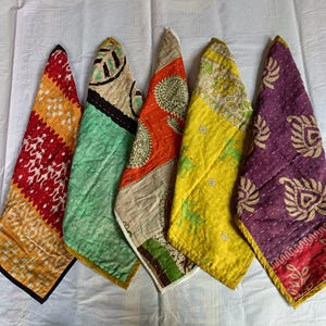Könnte beinhalten: Fünf farbenfrohe Stoffstücke mit verschiedenen Mustern sind zu sehen. Die Textilien zeigen geometrische, florale und Tiermotive in Rot-, Gelb-, Grün-, Orange- und Lilatönen. Sie sind auf einer weißen Oberfläche angeordnet.
