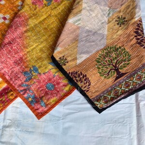 Pode incluir: Close-up de tr&ecirc;s t&ecirc;xteis coloridos estampados. Os tecidos apresentam desenhos florais e geom&eacute;tricos em tons de laranja, rosa, amarelo e castanho. As bordas s&atilde;o finalizadas com uma borda contrastante e costuradas com fio branco. Os t&ecirc;xteis parecem ser feitos &agrave; m&atilde;o.