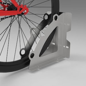 Op de afbeelding: Een zilveren metalen fietsstandaard met een zwarte fietsband. De standaard heeft een driehoekig ontwerp met meerdere gaten en sleuven. Het fietsframe is rood.