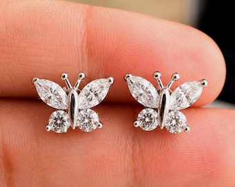 May include: A pair of silver-toned butterfly stud earrings featuring clear, faceted marquise-cut and round-cut stones. Each earring is shaped like a butterfly with two marquise-cut stones forming the upper wings and two round-cut stones forming the lower wings.