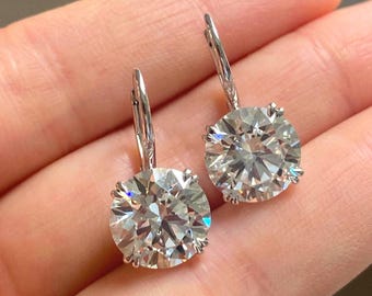 May include: A pair of silver-toned leverback earrings, each featuring a large, round, brilliant-cut clear stone set in a four-prong setting. The stones exhibit significant light refraction and sparkle, suspended from secure, hinged metal closures.