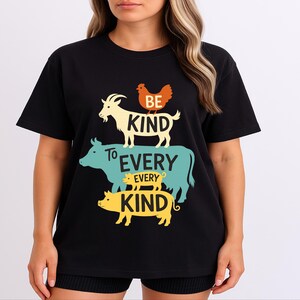 Pode incluir: Camiseta preta com um design gráfico com uma cabra, uma galinha, uma vaca, um porco e as palavras "BE KIND TO EVERY KIND" em uma disposição empilhada. O design usa cores amarelo, laranja e turquesa.