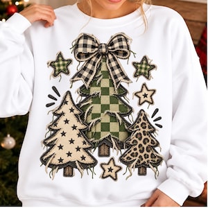 May include: A white long-sleeve sweatshirt featuring a central graphic of three Christmas trees with frayed edges. The trees display a green checkered pattern, a black star print on beige, and a leopard print. A black and white buffalo plaid bow sits atop the center tree, surrounded by four small stars.