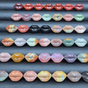 May include: A collection of forty-two small, carved stone lip-shaped beads arranged in six horizontal rows. The beads feature a variety of colors including shades of red, pink, green, orange, black, purple, and tan, with some showing marbled patterns.