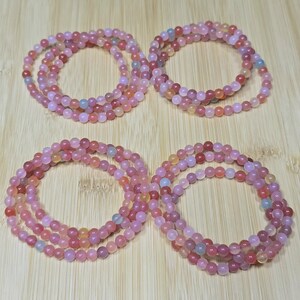 May include: Four circular bracelets made of small, smooth, translucent pink and reddish-orange gemstone beads. Each bracelet consists of a single strand of round beads, displaying variations in color intensity and subtle internal inclusions.