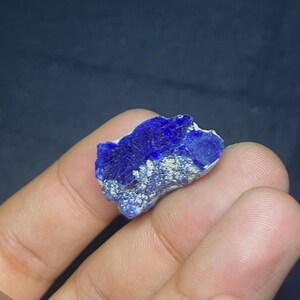 May include: A vibrant blue lapis lazuli gemstone with a rough, textured surface. The stone has a deep, saturated color with lighter, speckled areas. The irregular shape and natural variations highlight its raw, unpolished state. This gemstone is ideal for jewelry making or collecting.