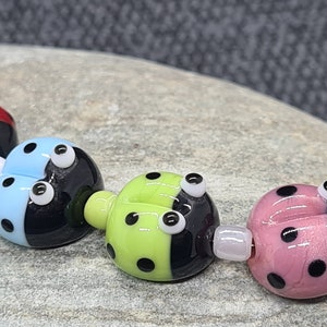 May include: A string of five glass ladybug beads, each with black and white eyes and black spots. The beads are in a rainbow of colours: yellow, red, blue, green, and pink.