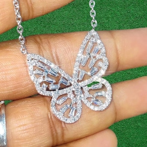Peut inclure: Un collier pendentif papillon argent&eacute; avec une cha&icirc;ne d&eacute;licate. Le pendentif papillon est incrust&eacute; de pierres pr&eacute;cieuses claires et &eacute;tincelantes. Le collier est pr&eacute;sent&eacute; sur un fond vert.