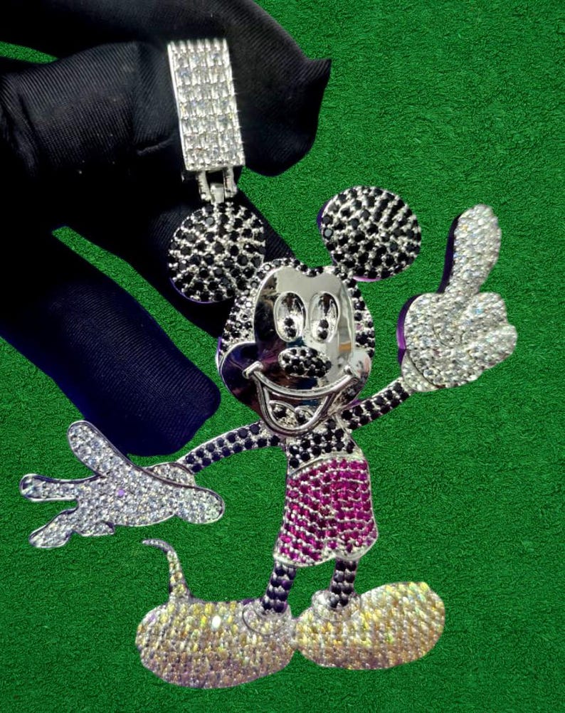May include: A silver-toned pendant in the shape of Mickey Mouse, encrusted with sparkling crystals and black accents. The pendant features a thumbs-up gesture and a smiling face, with a matching bail at the top for a chain.