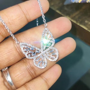 Peut inclure: Un collier pendentif papillon argent&eacute;. Le motif papillon est incrust&eacute; de petits cristaux &eacute;tincelants. La cha&icirc;ne du collier est d&eacute;licate et &eacute;galement argent&eacute;e. Le collier est pr&eacute;sent&eacute; sur un fond neutre.